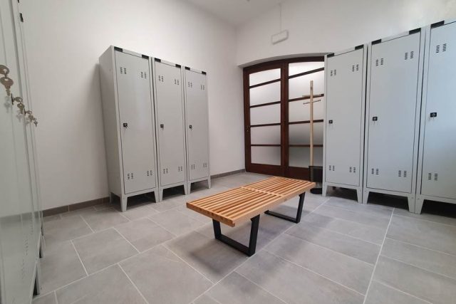 Spogliatoio aziendale con armadietti personali metallici e panchina di design.
