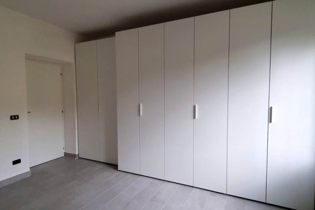 Armadio su misura a battente realizzato con doppia profondità. Finitura laminato bianco.